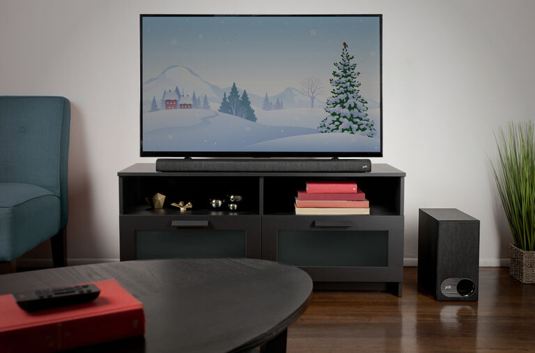 A room with a TV and sound bar sitting on a TV stand. A subwoofer is on the floor next to them. A room with a TV and sound bar sitting on a TV stand. A subwoofer is on the floor next to them.