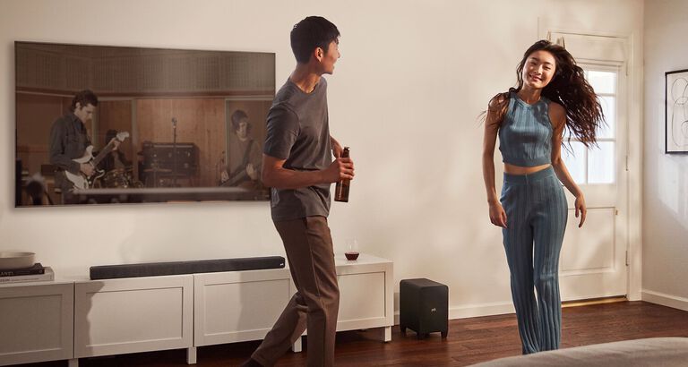 A family sitting in a room. A man controls a sound bar with a remote. A family sitting in a room. A man controls a sound bar with a remote.